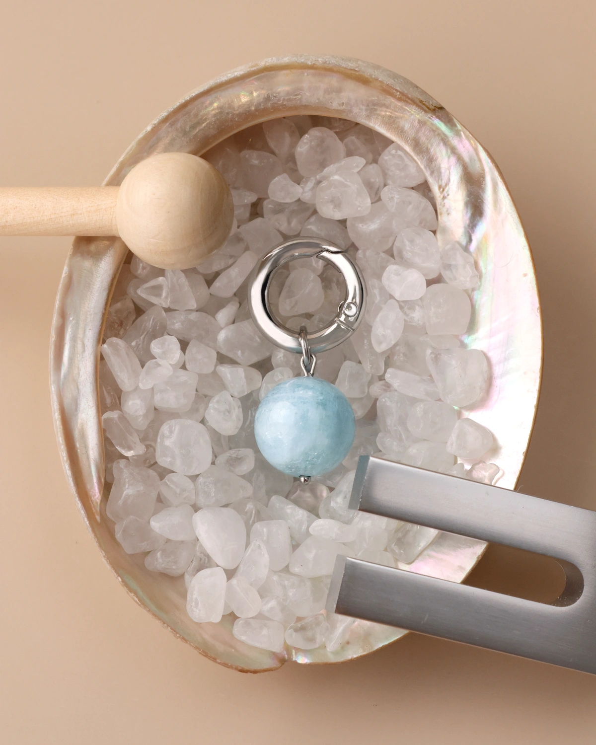 Aquamarine charm resting in an abalone shell filled with quartz chips