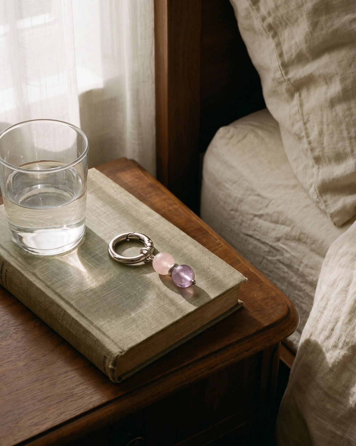 LuStar charm with rose quartz and amethyst beads on a linen book by a glass of water