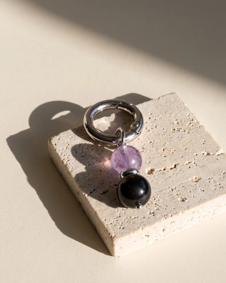 LuStar charm with amethyst and obsidian beads on a travertine block in hard sunlight