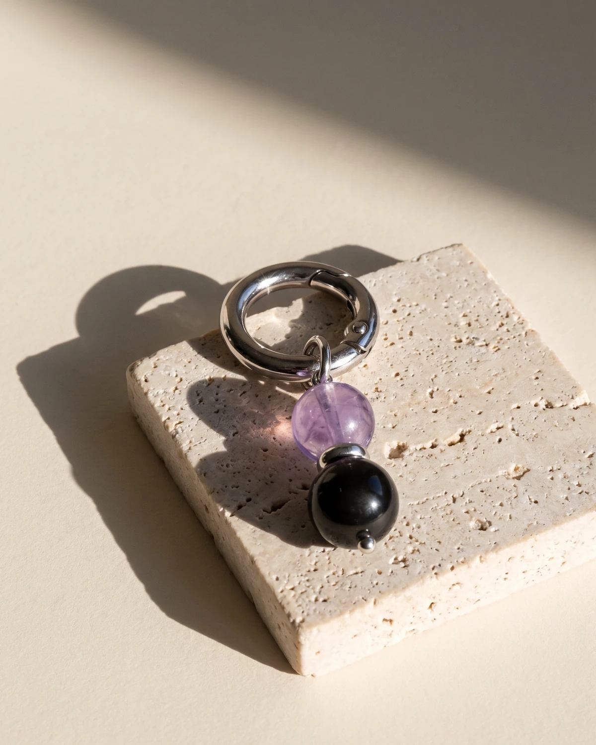 LuStar charm with amethyst and obsidian beads on a travertine block in hard sunlight