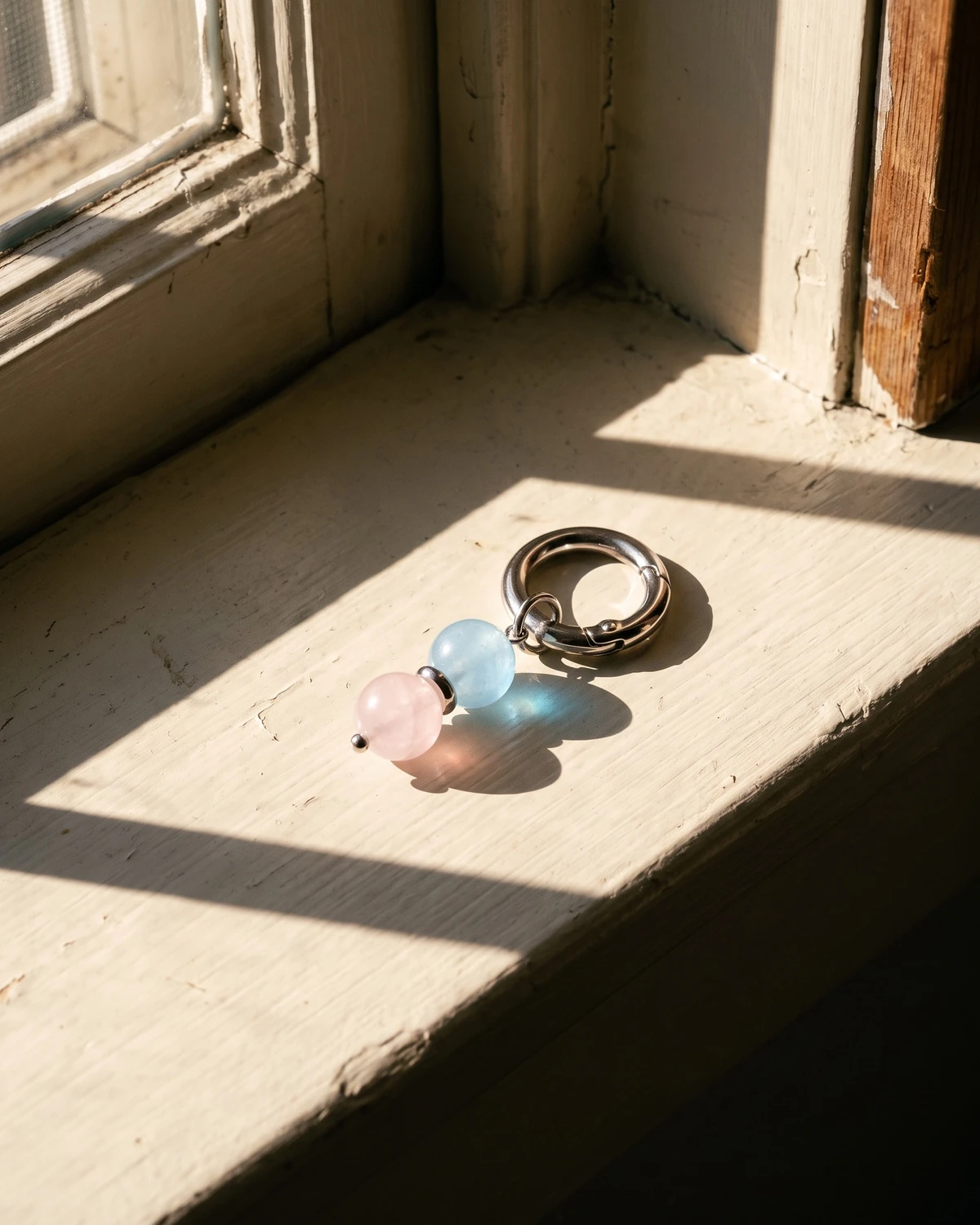 LuStar charm with aquamarine and rose quartz beads on a sunlit windowsill